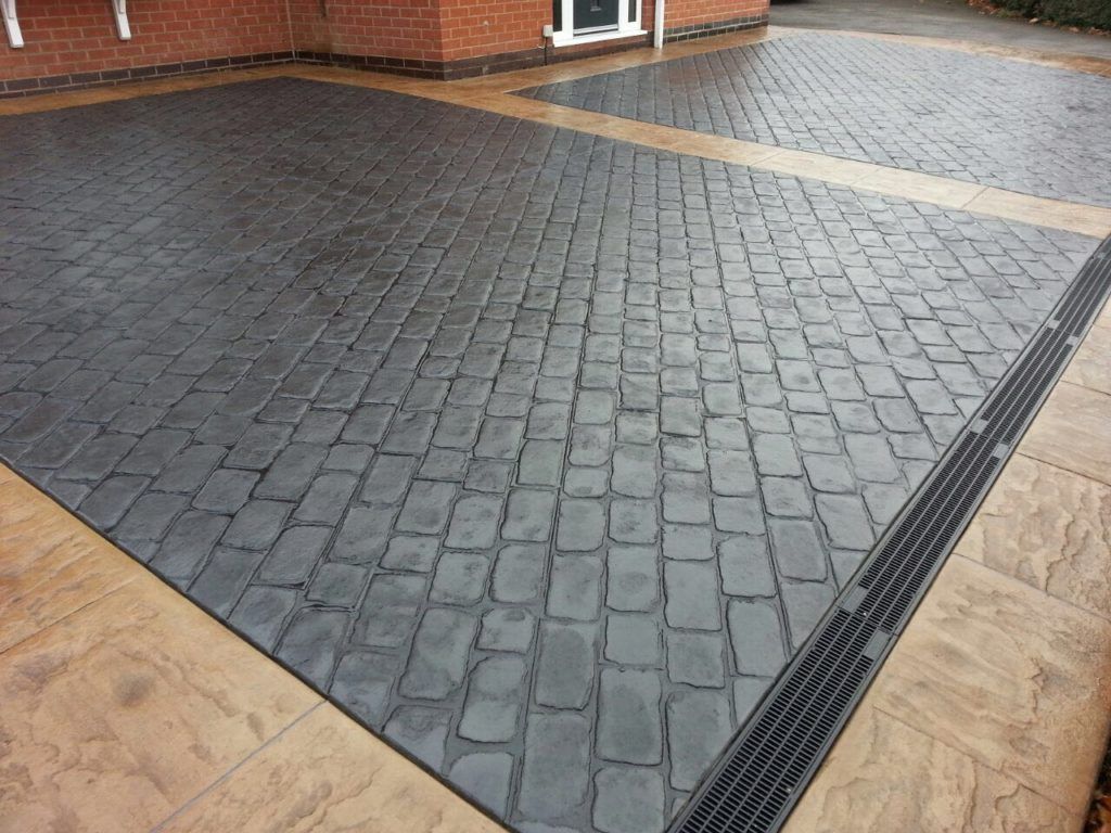 Charcoal cobble pattern imprinted concrete with a sandstone border and drainage channel