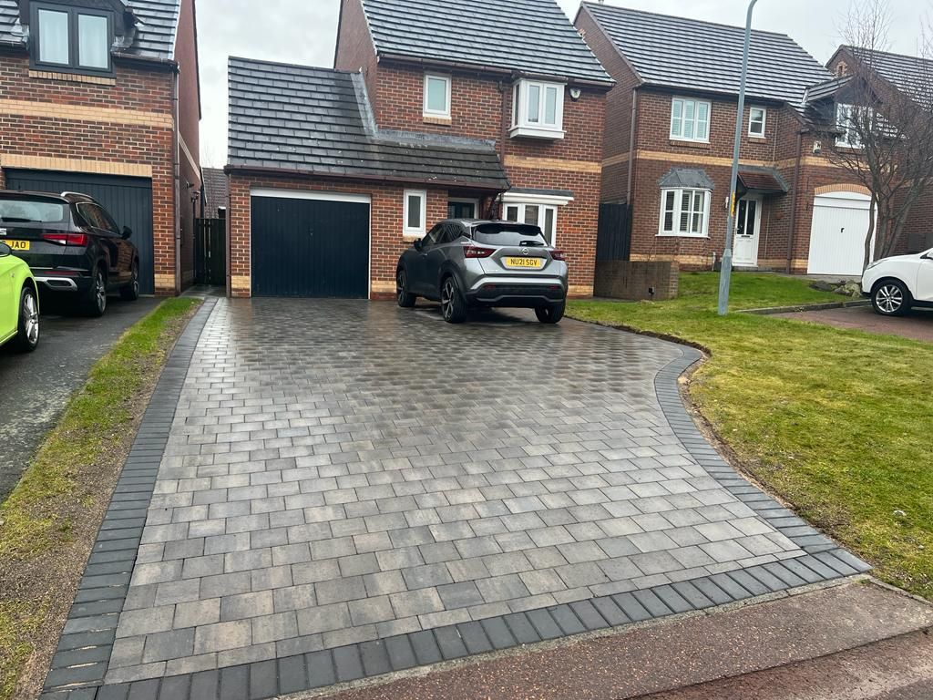 Tumbled block paving with a charcoal border and a curved edge onto the lawn