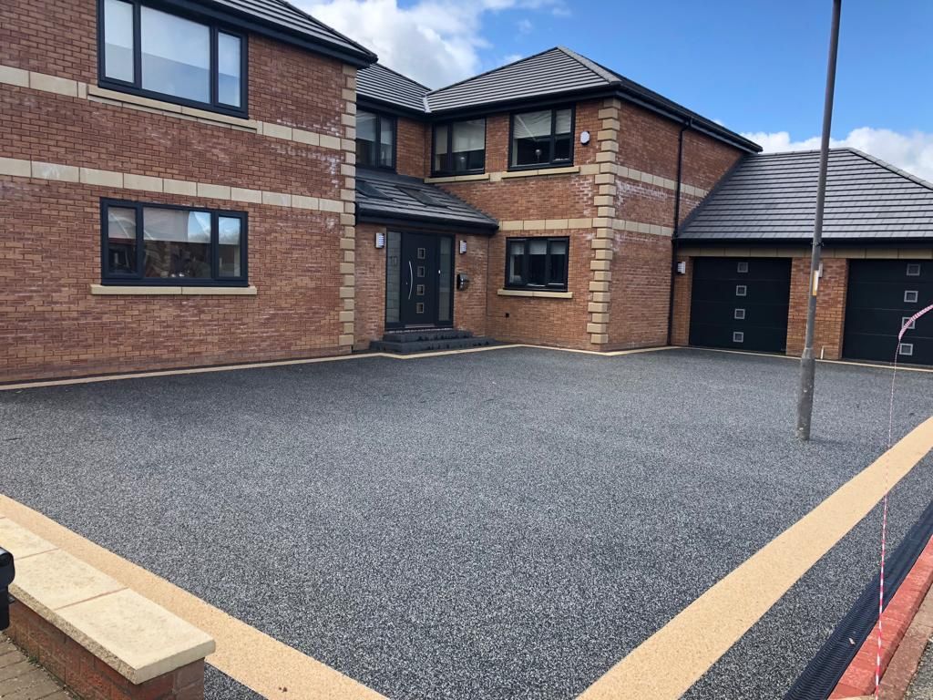 Large charcoal resin bound driveway with a cream border and double garage