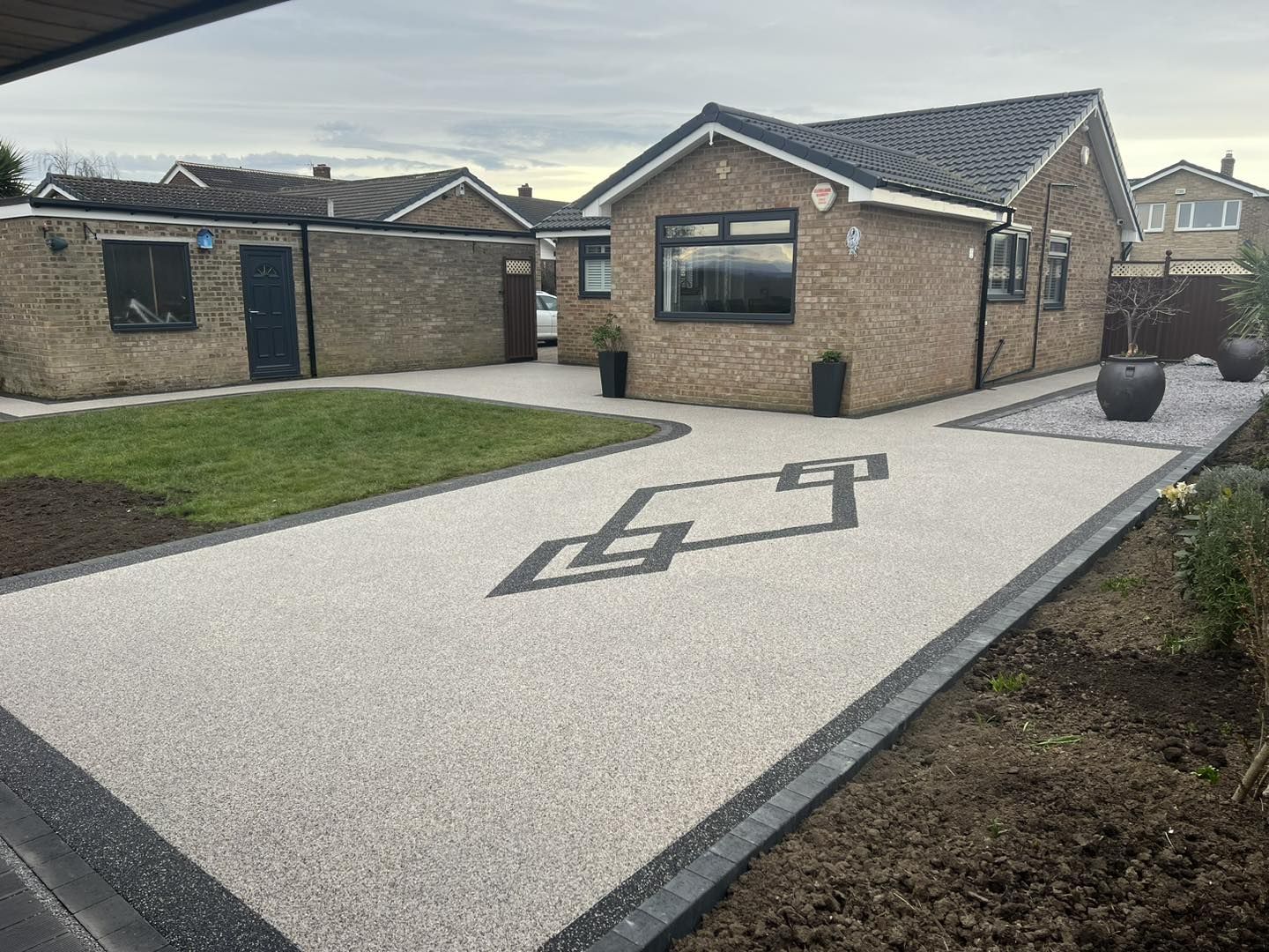 Oyster resin bound driveway with a bespoke geometric inlay and charcoal kerb
